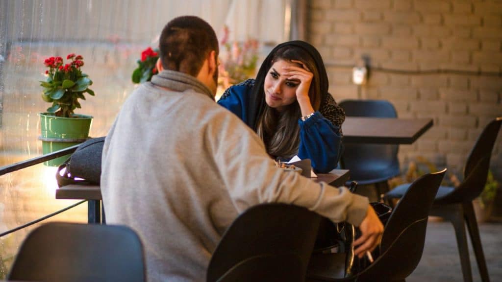 A woman rests her head on her hand while looking at a man across a table.