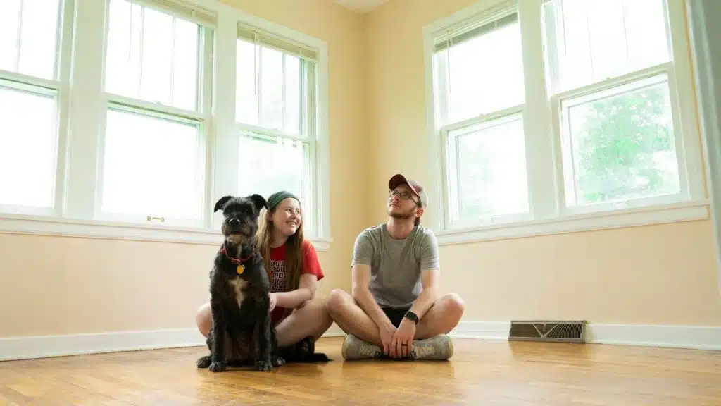 A couple sitting on the floor with their dog in an empty room.