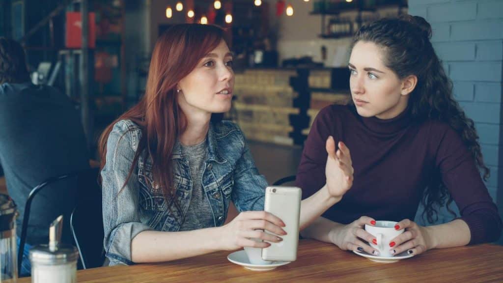A woman explaining something to a friend across a café table.