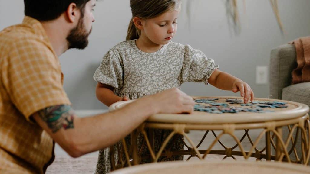 A man and young girl playing a puzzle together at a small table.