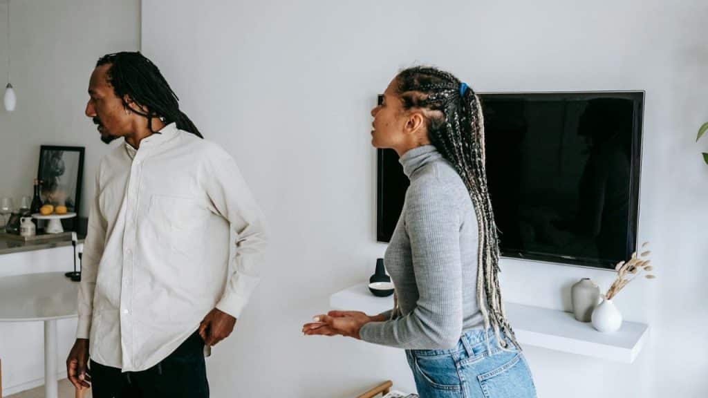 A woman with long braids gestures toward a man who is walking away from her.