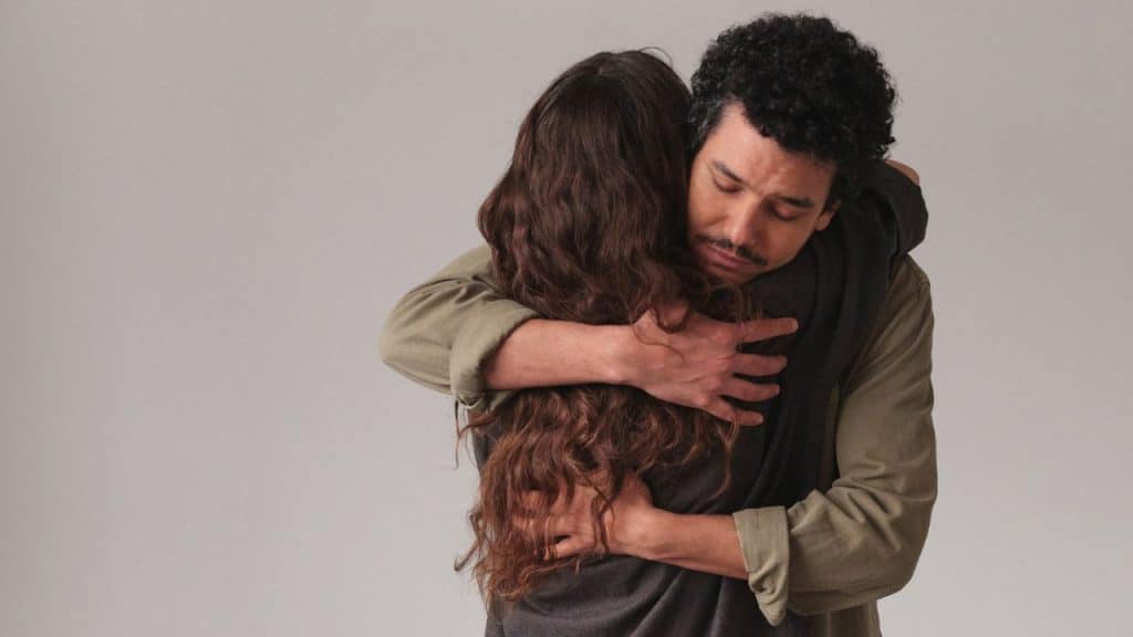 A man with curly hair closes his eyes while embracing a woman with long hair.