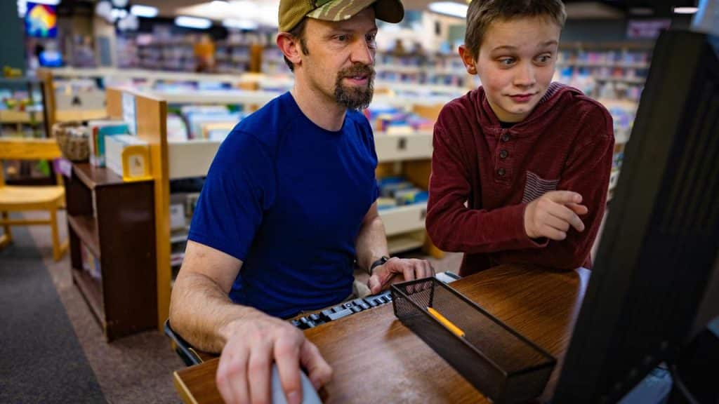 A man and a boy using a computer together in a library or bookstore.