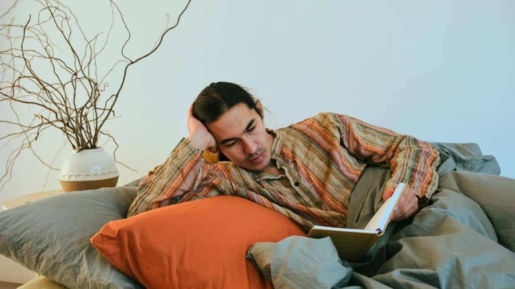 A person reclining on a bed while reading a book in a calm, cozy room.