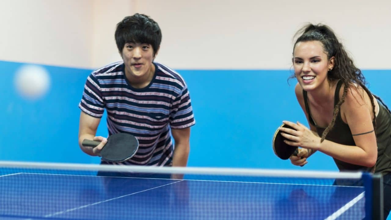 A man and a woman hold paddles while playing a game of table tennis.