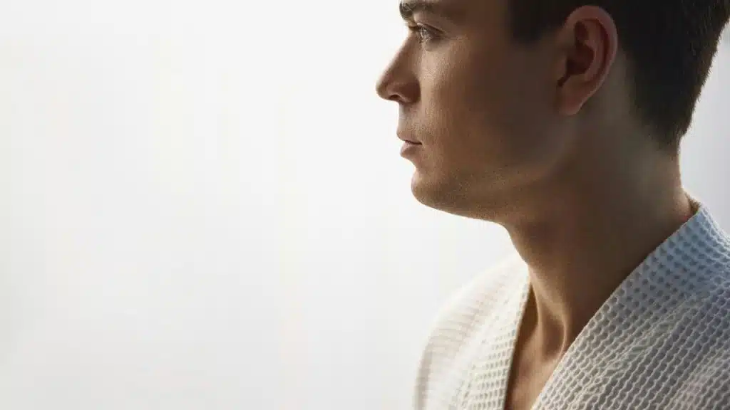 A person in profile looking thoughtfully toward a bright background.