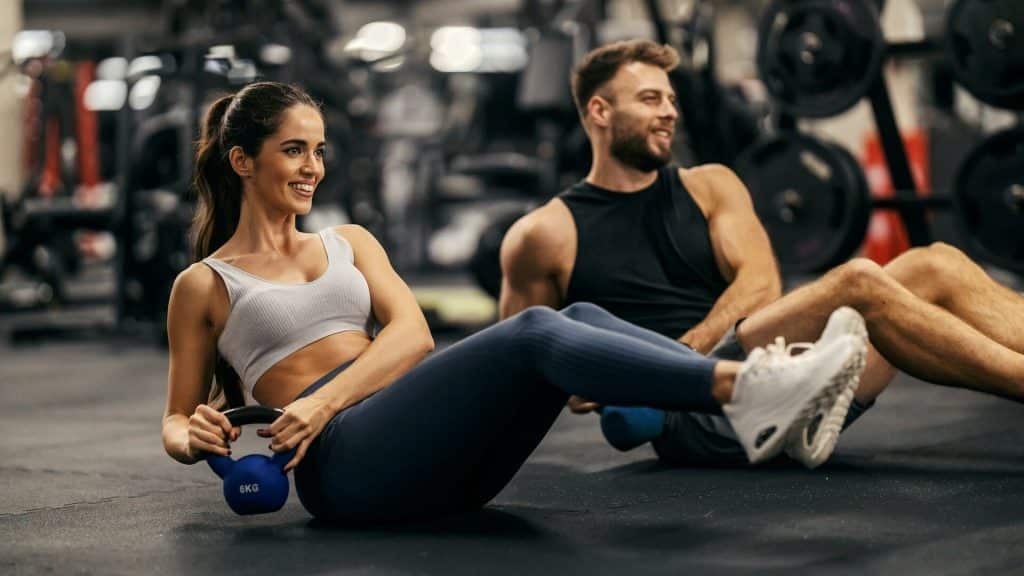 A fit sporty couple doing kettlebell exercises in the gym.