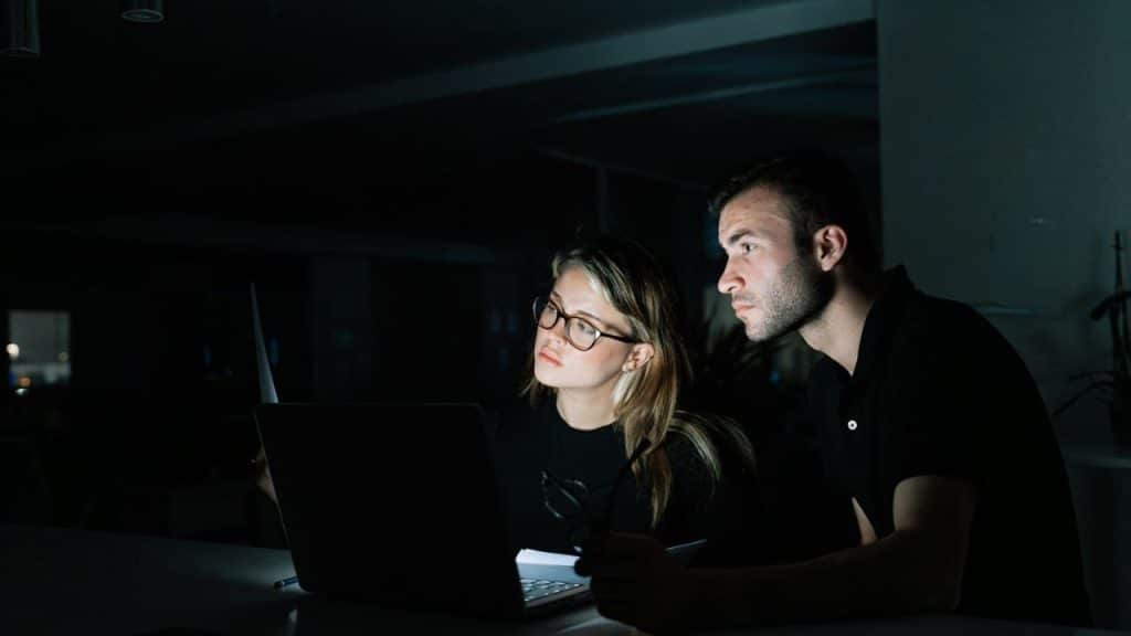 A man and woman look at a laptop screen together in a dark room.