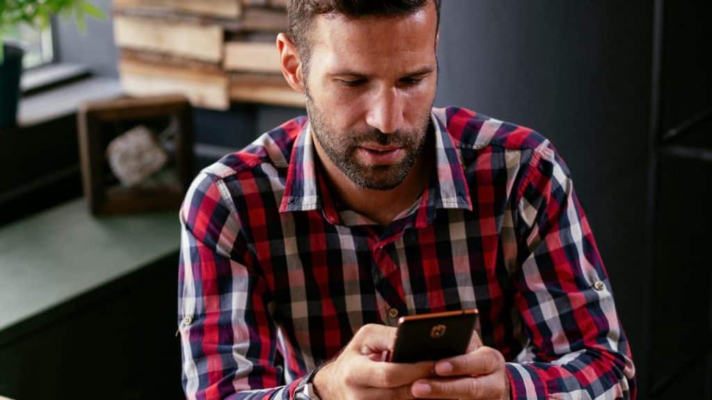 A man in a red and black plaid shirt looks down while holding a smartphone.