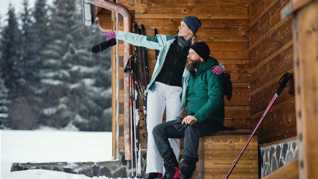 A couple resting by the wooden hut after skiing.