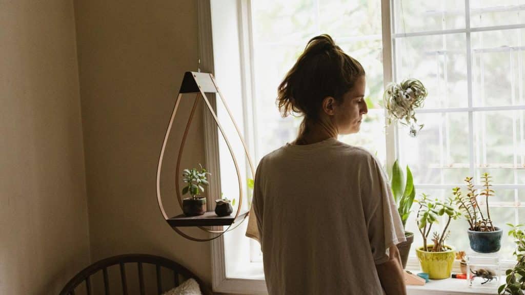 A person standing by a sunlit window, tending to small potted plants indoors.