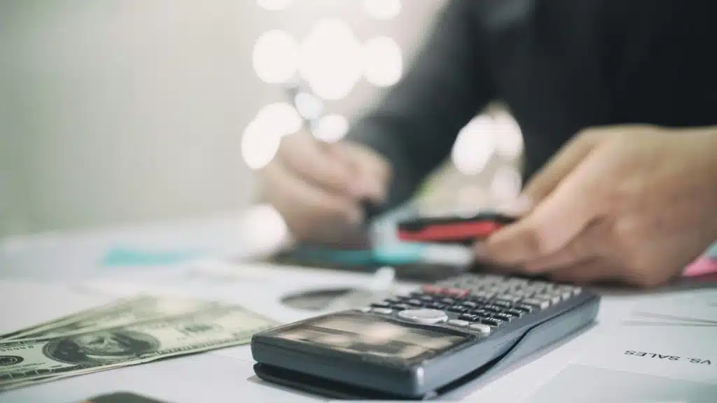 A person using a calculator with cash and cards on the table.