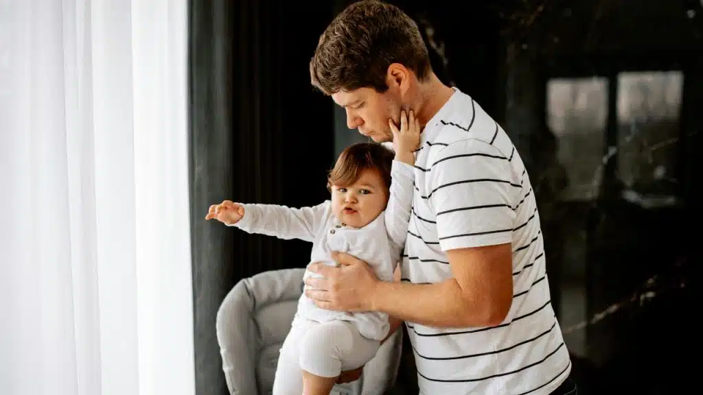 A father holding his child near a window.