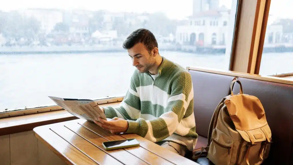 A man reading a map while sitting by a window on a boat.