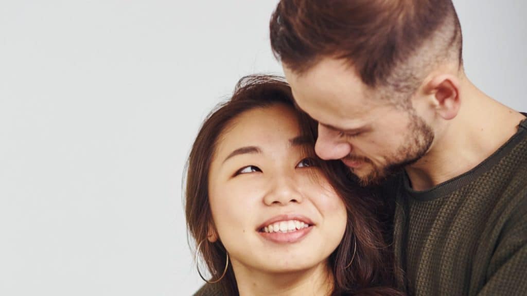 A woman smiling and looking at a bearded man as he holds her tightly.