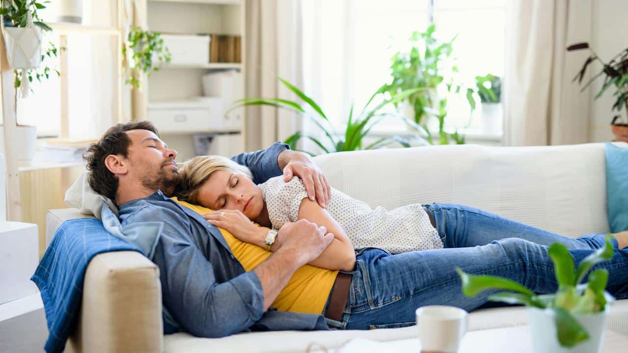 A couple napping together on a white couch at home.