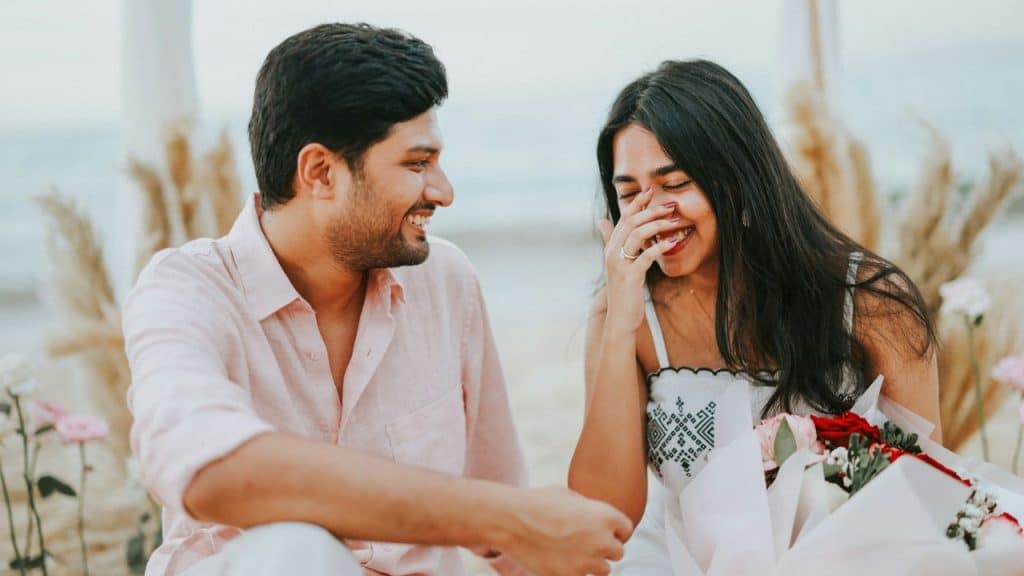 A woman laughs with her hand over her mouth while a man smiles at her.