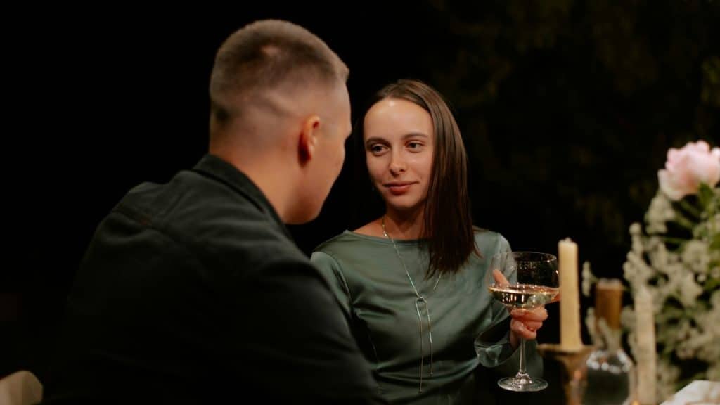 A woman in a green dress holds a wine glass while looking at a man.