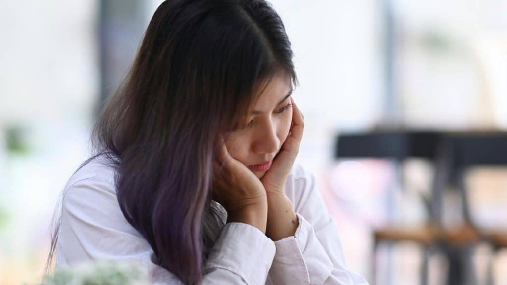 A woman resting her face in her hands while sitting indoors.