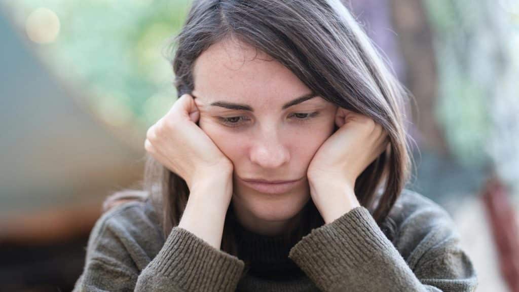 A woman resting her face in her hands, looking down with a pensive expression.