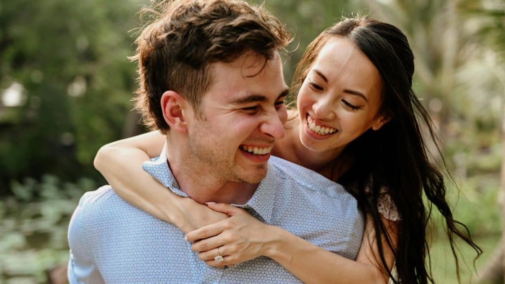 A couple laughing outdoors while sharing a playful embrace.