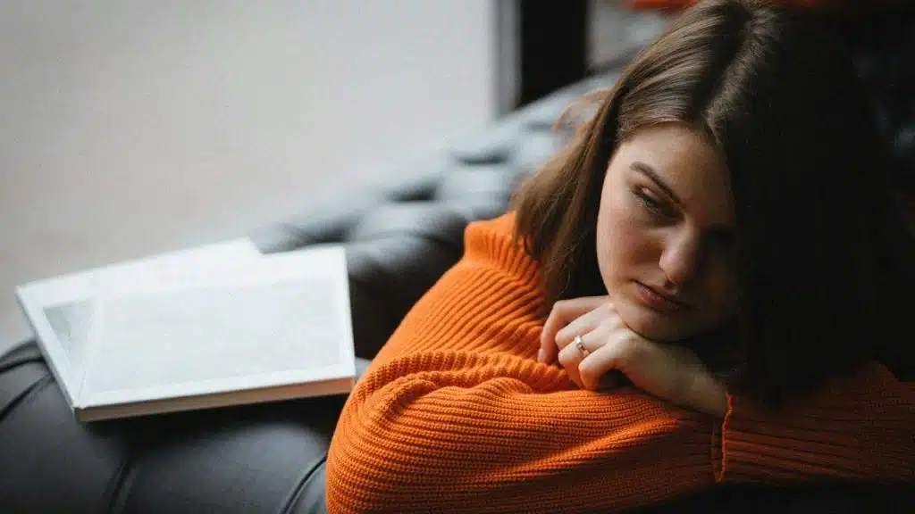 A woman resting her head on her arms beside an open book.