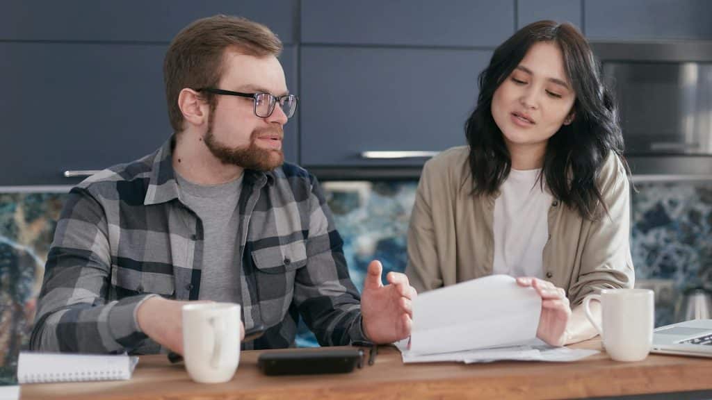 A couple sitting at a wooden table having a conversation about finances.