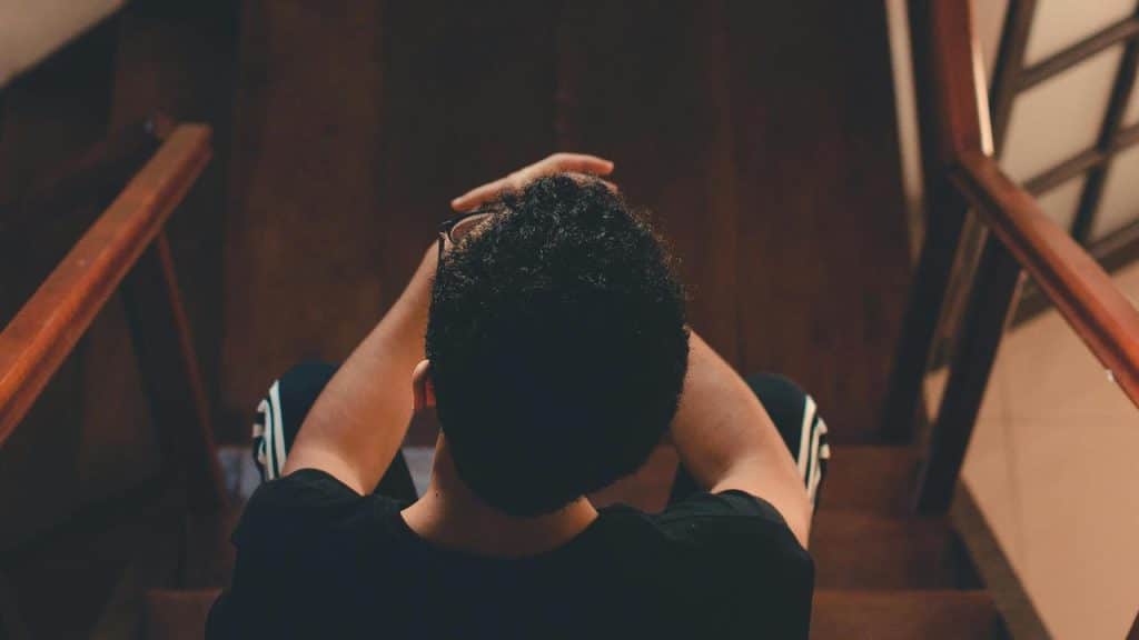 A person sitting on stairs with hands on their head.