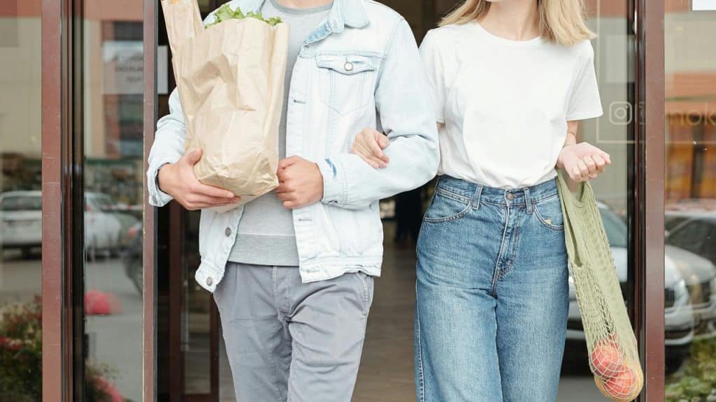 A couple walks out of a store carrying grocery bags.
