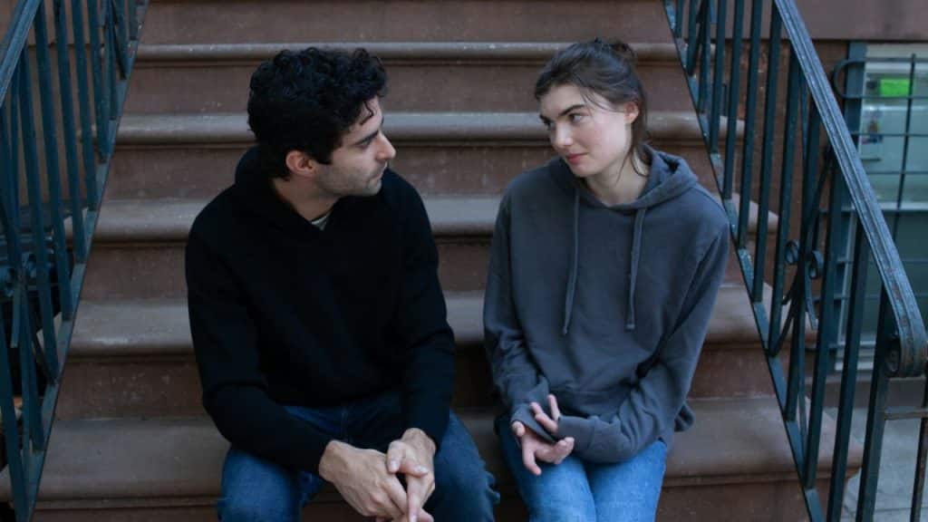 A man and woman sit on outdoor concrete stairs, looking at each other and talking.