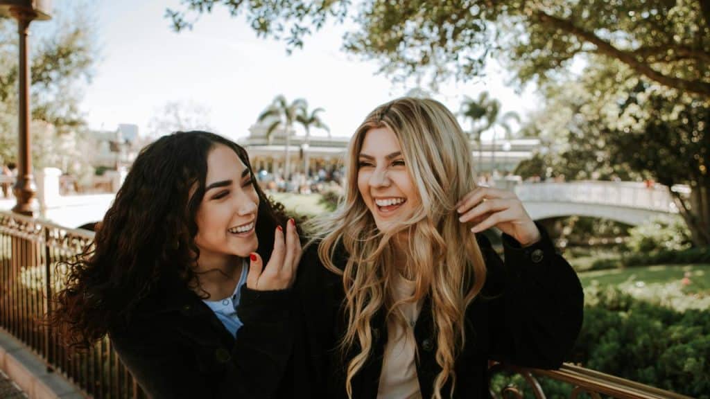 A pair of friends laughing together outdoors near a park bridge.