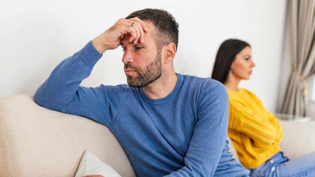 A man sits on a couch with his head in his hand while a woman looks away.