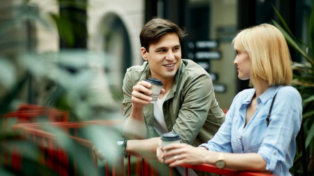 A man in a green shirt smiles while holding a coffee cup next to a woman.