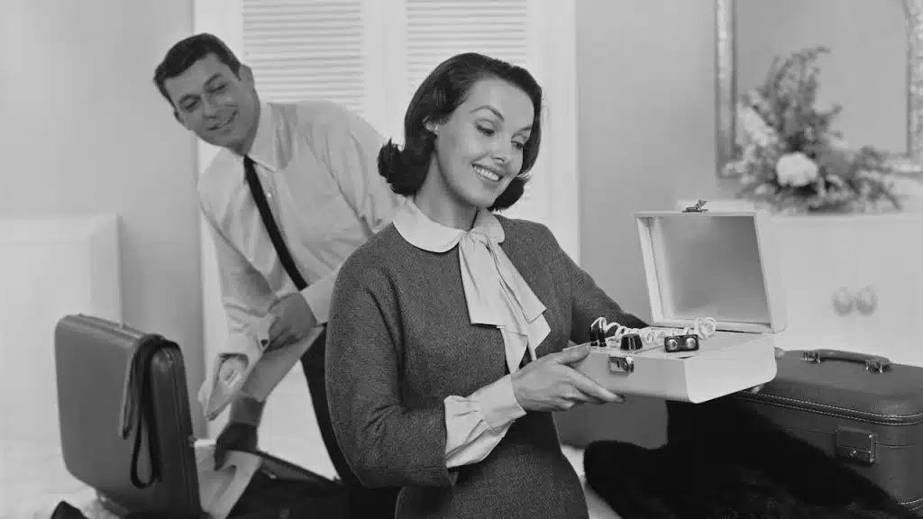 A black-and-white photo of a woman opening a suitcase while her husband is packing his suitcase.