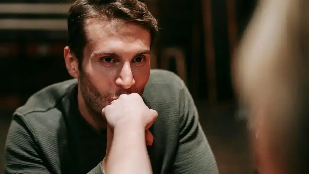 A man in a green shirt leans forward while holding another person's hand to his mouth.