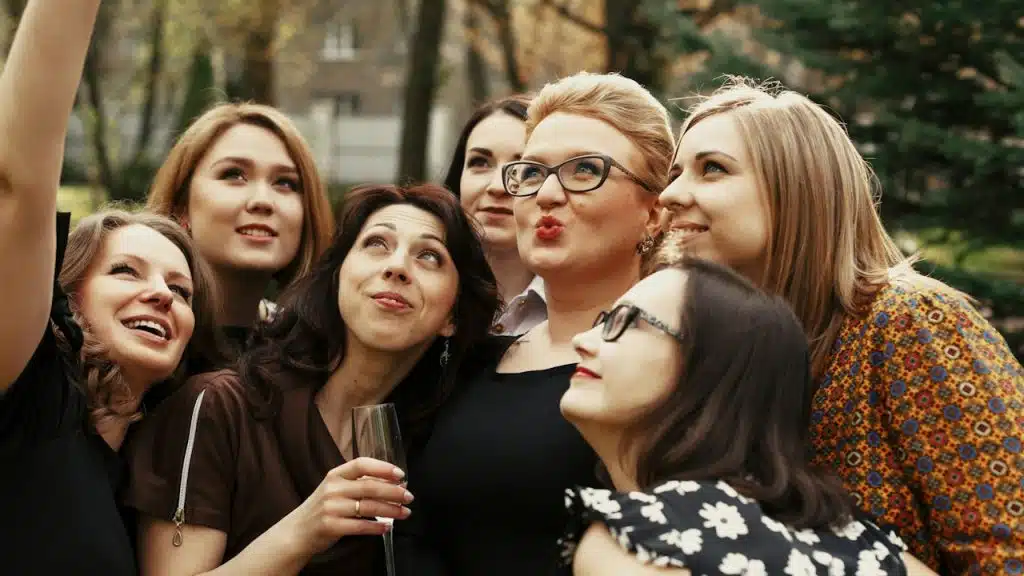 A group of stylish young ladies taking a selfie at a gathering in a park.