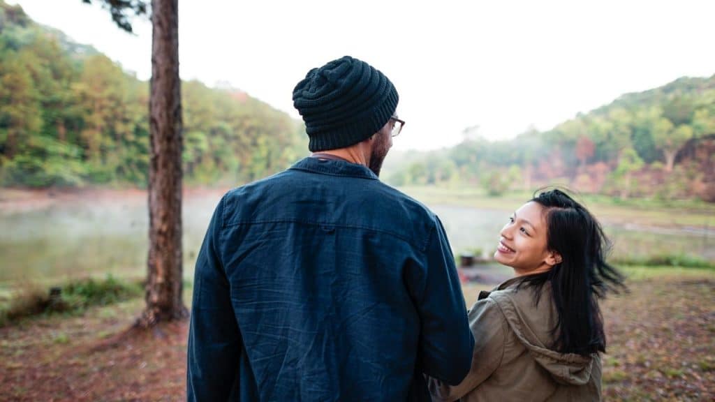 A couple walking outdoors by a misty lake, sharing a quiet moment together.