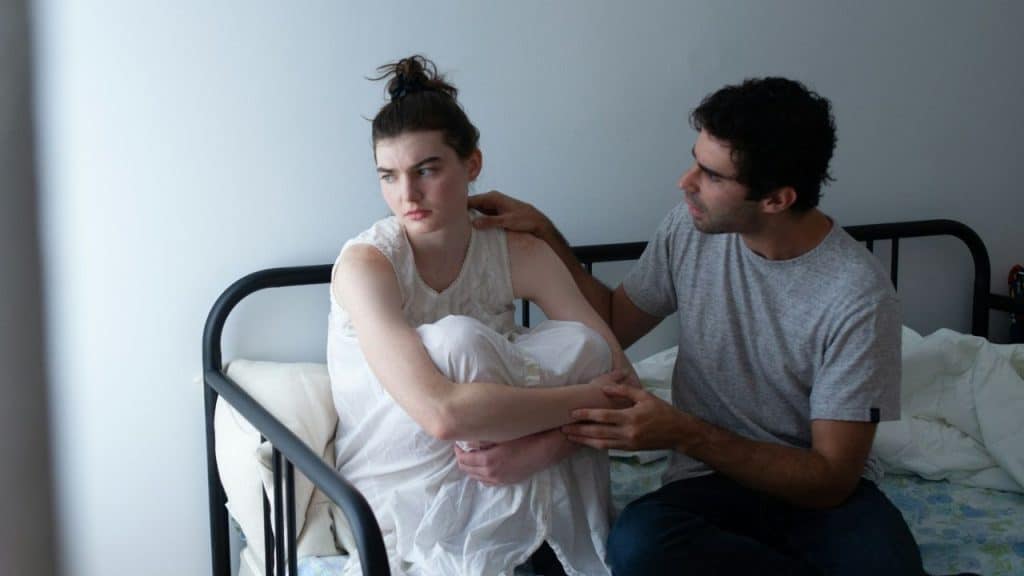 A man reaches out to touch a woman who is sitting with her knees tucked.