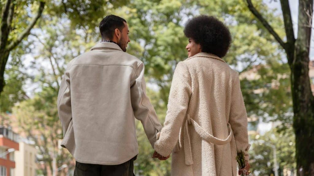 A couple holding hands while walking through a tree-lined street.
