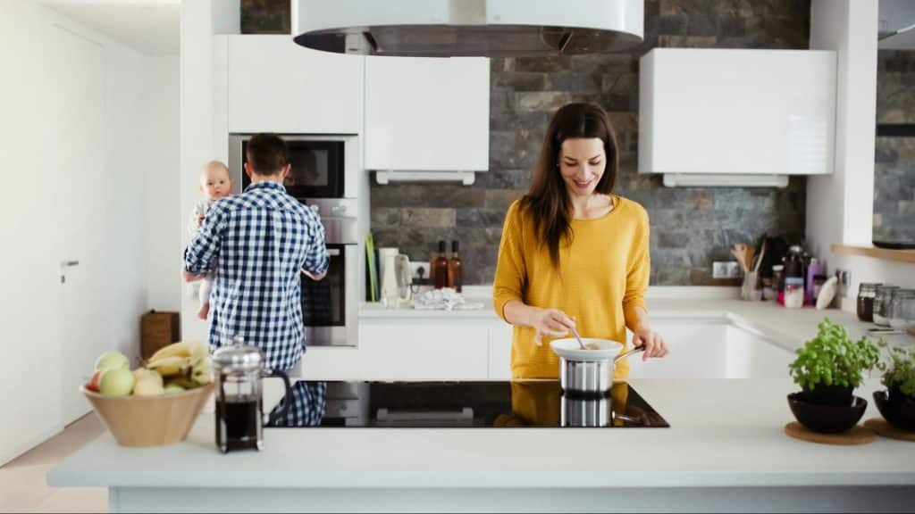 A man carrying a child while a woman cook for them