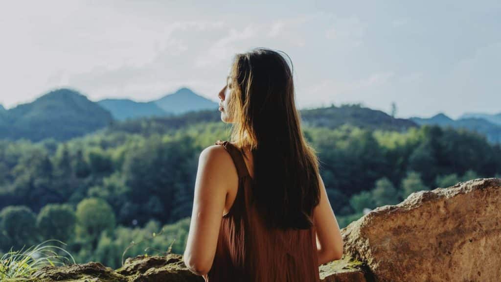 A woman gazing over a forested mountain landscape from a rocky overlook.