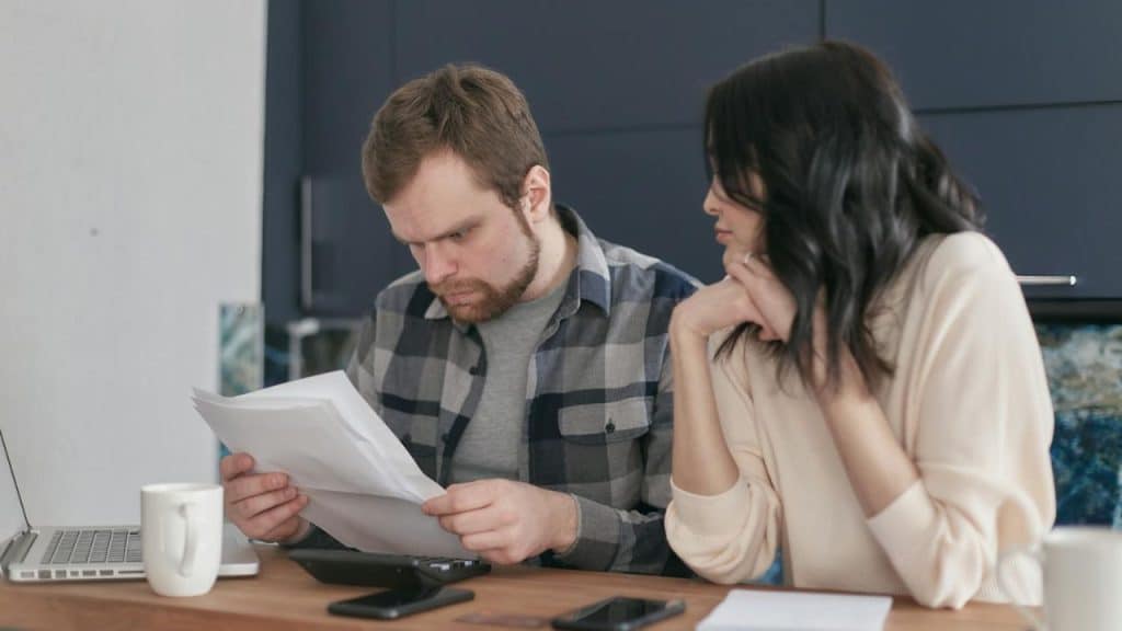 A man in a plaid shirt reviews papers while a woman sits beside him watching.