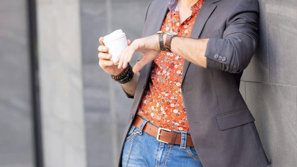 A person holding a coffee cup while checking a wristwatch outdoors.