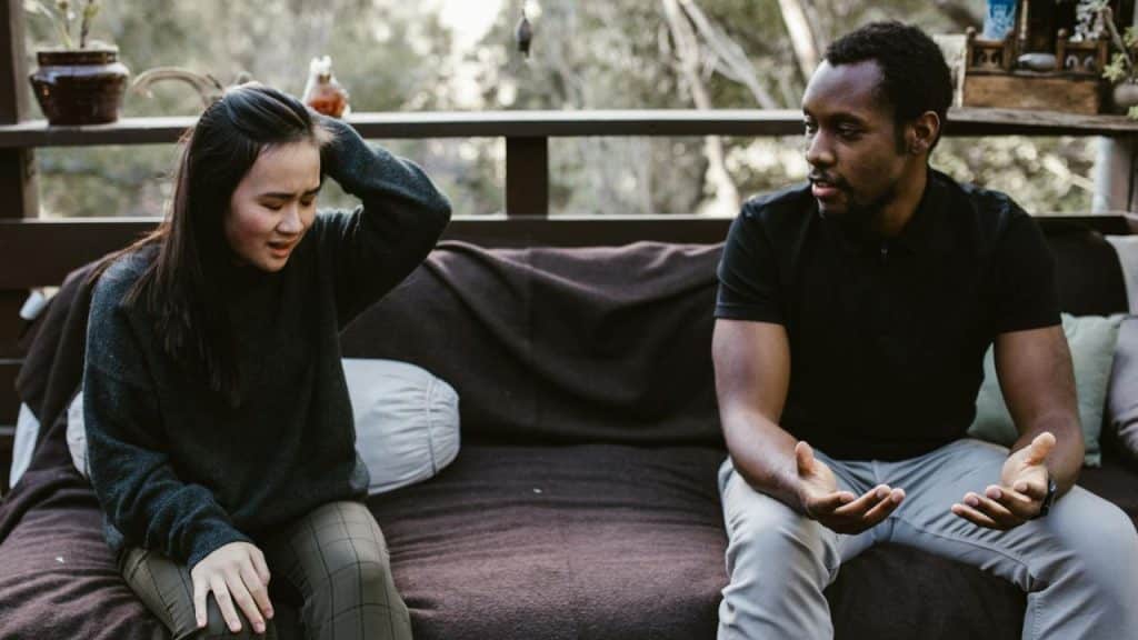 A man and woman in plaid shirts sit on a couch having a serious discussion.