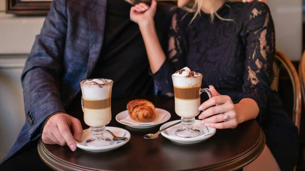A couple enjoying layered coffee drinks and a pastry at a café table.