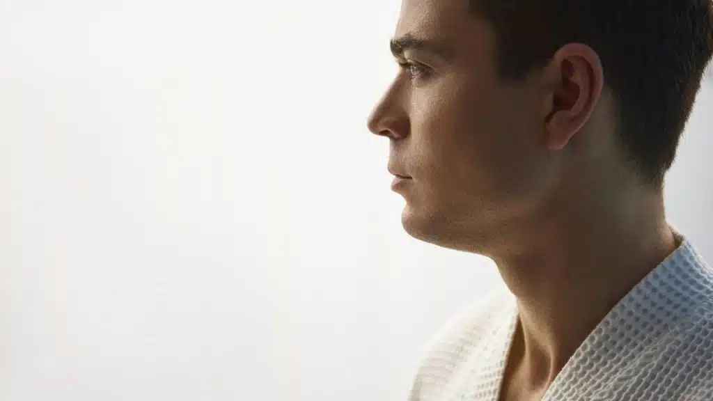 A man in a white robe is shown in profile, looking forward against a plain background.
