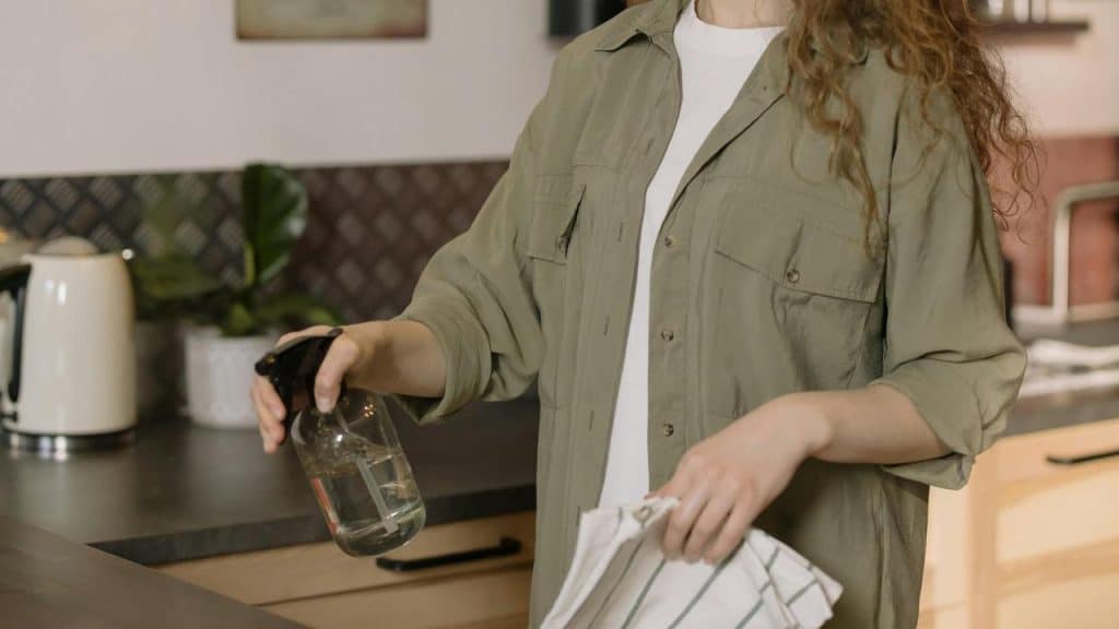 A person holding a spray bottle and cloth while cleaning a kitchen counter.