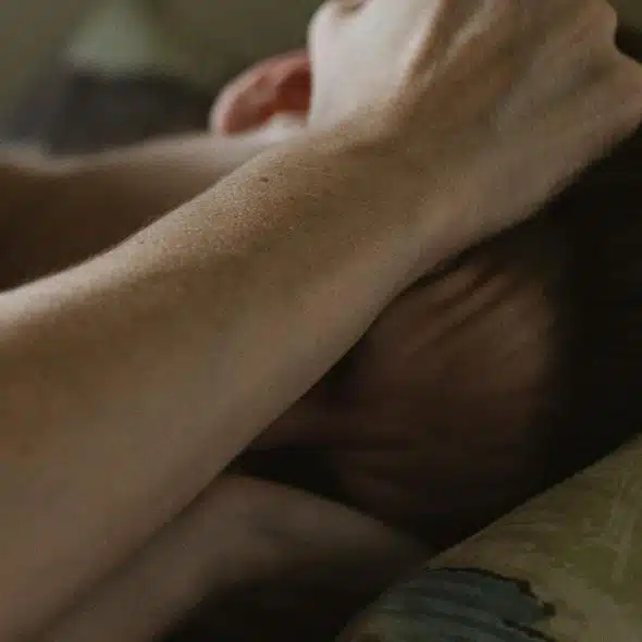 A person lying in bed with an arm covering their face.