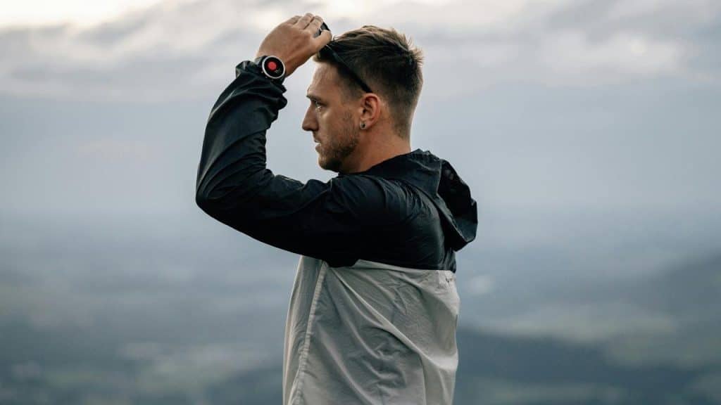 A man in a jacket adjusting his headwear outdoors.