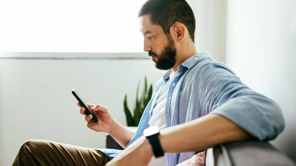 A man sitting on a couch while looking at his smartphone.